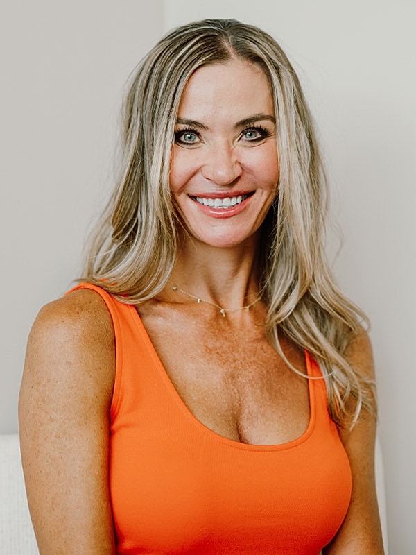 Smiling woman in orange tank top against wall.