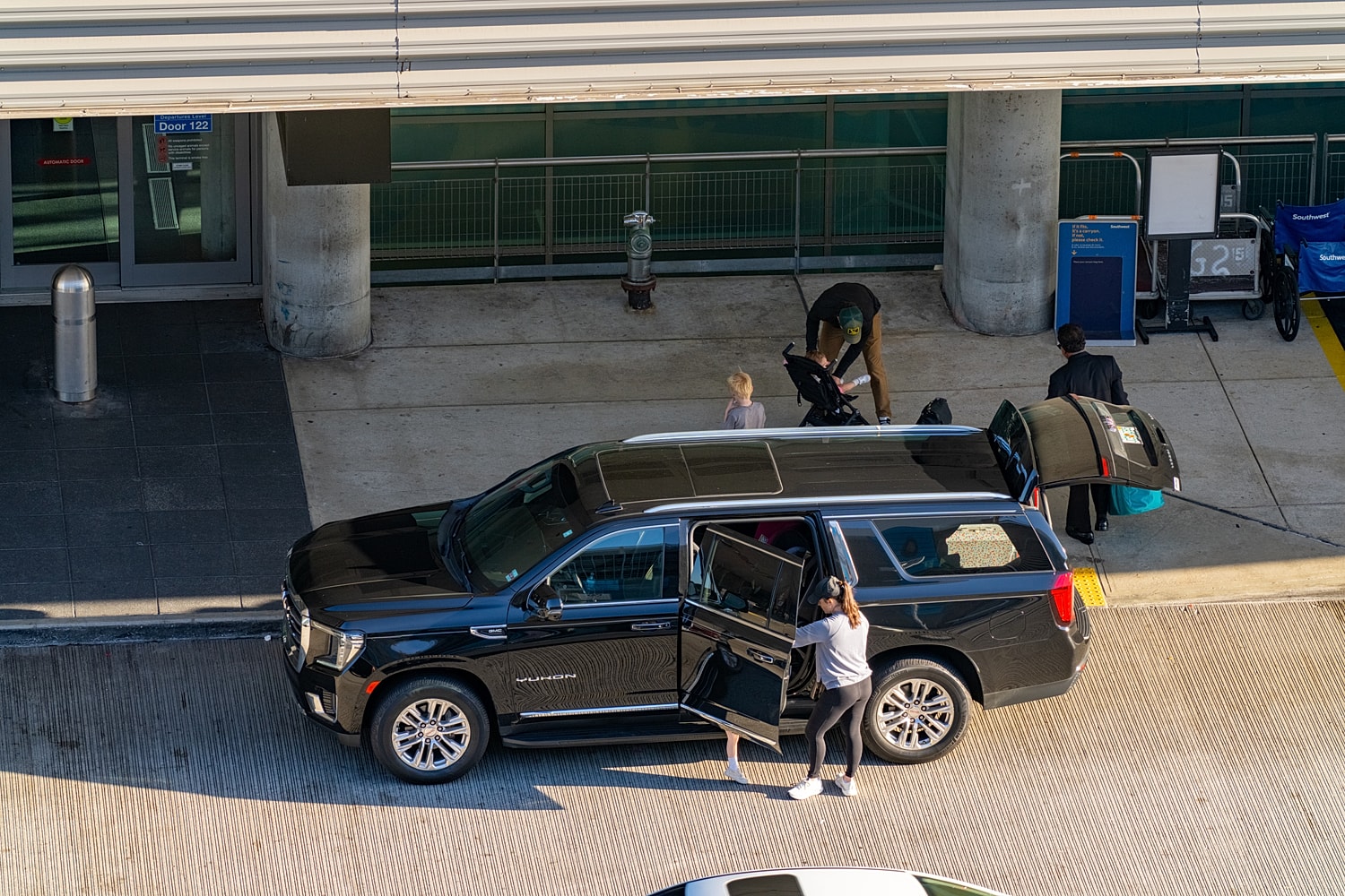 Family unloading luggage at airport drop-off.