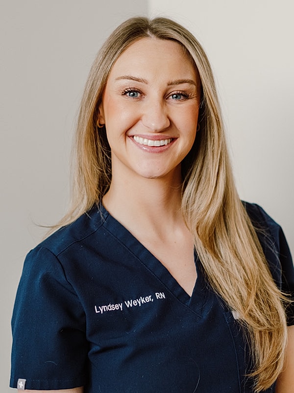Smiling nurse in professional scrubs against neutral background.