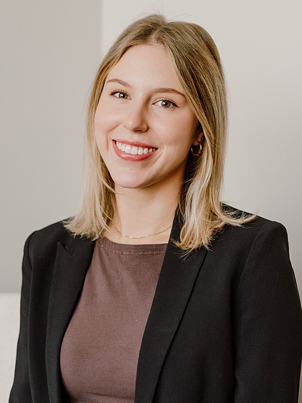 Smiling woman in professional attire against neutral background.